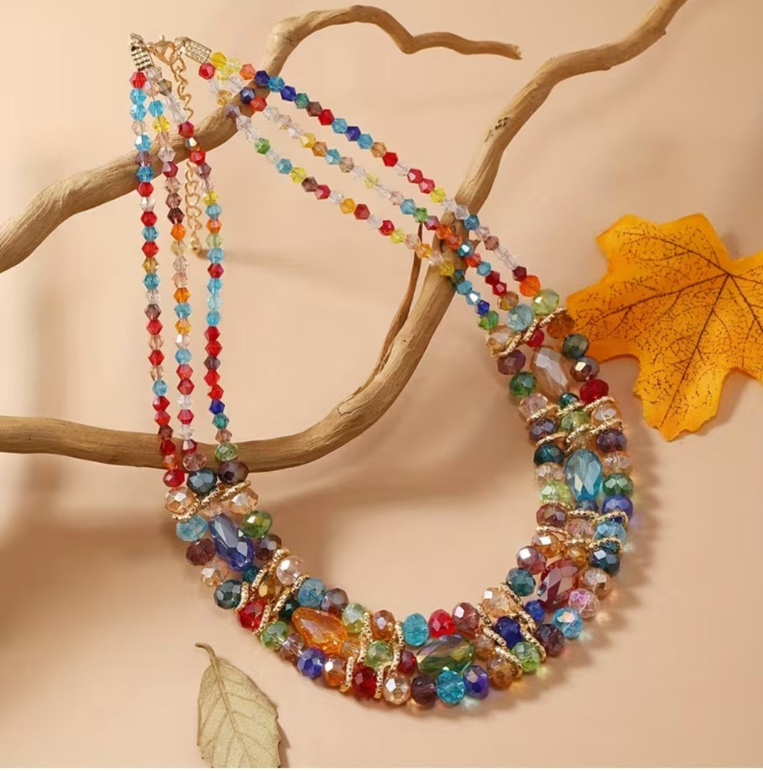 Designed with three cascading rows of beads, it creates a layered effect that adds depth and movement to any outfit. Each bead is uniquely colored, blending earthy tones with bright pops of multicolor for a playful yet sophisticated look.