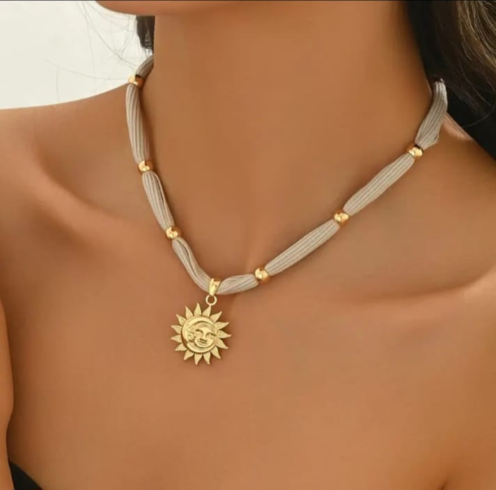 This radiant necklace showcases a luminous gold sun pendant gracefully woven between strands of soft fabric, creating a unique blend of elegance and comfort.