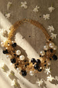 Multi‑layered clavicle necklace featuring rich tons of gold, deep black, and faux pearl