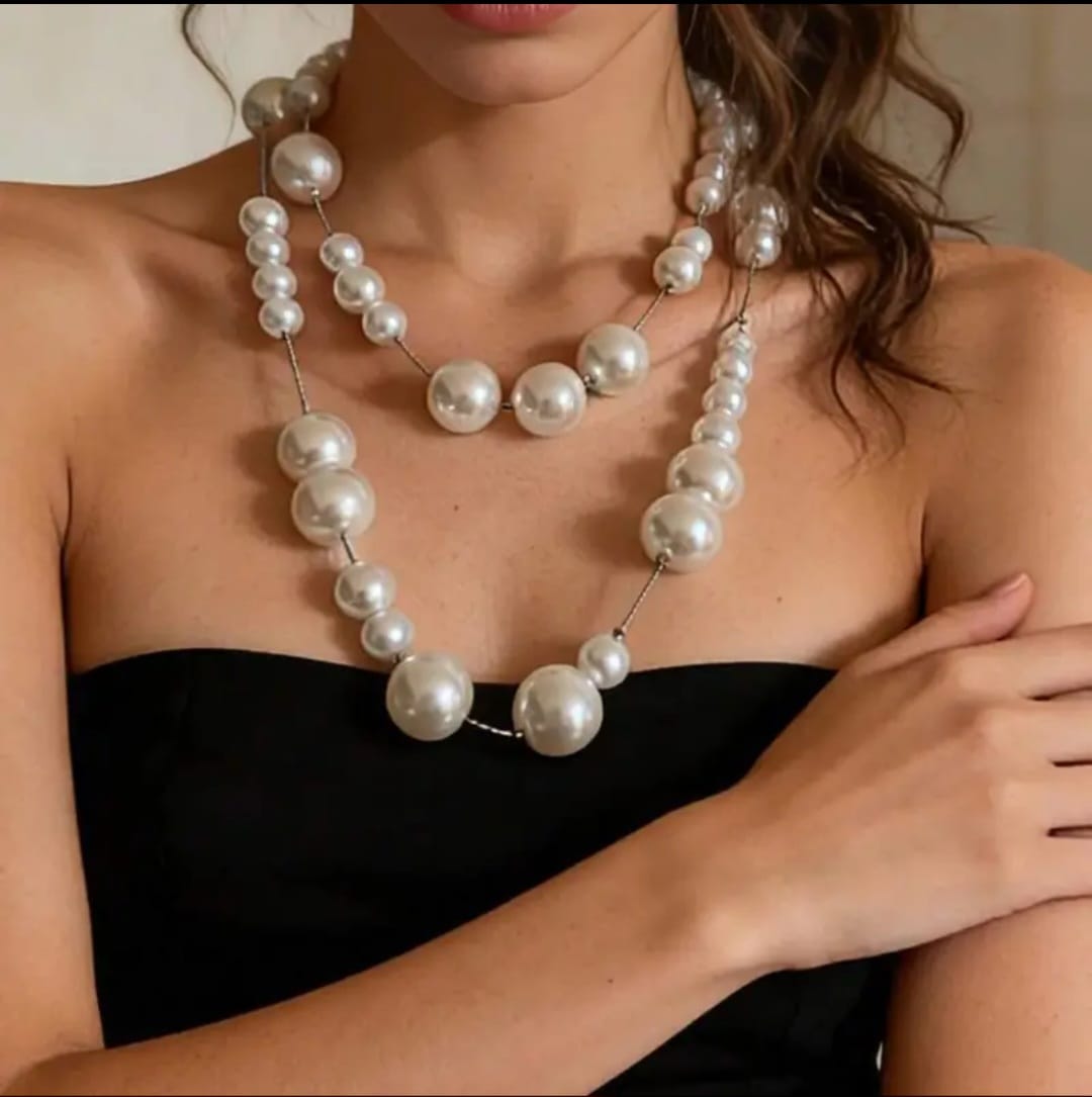 A silver long necklace with large synthetic pearl beads is a striking piece of jewelry that combines classic elegance with modern design. The polished silver chain glimmers softly as it drapes gracefully down the chest, creating a fluid line that elongates the silhouette.